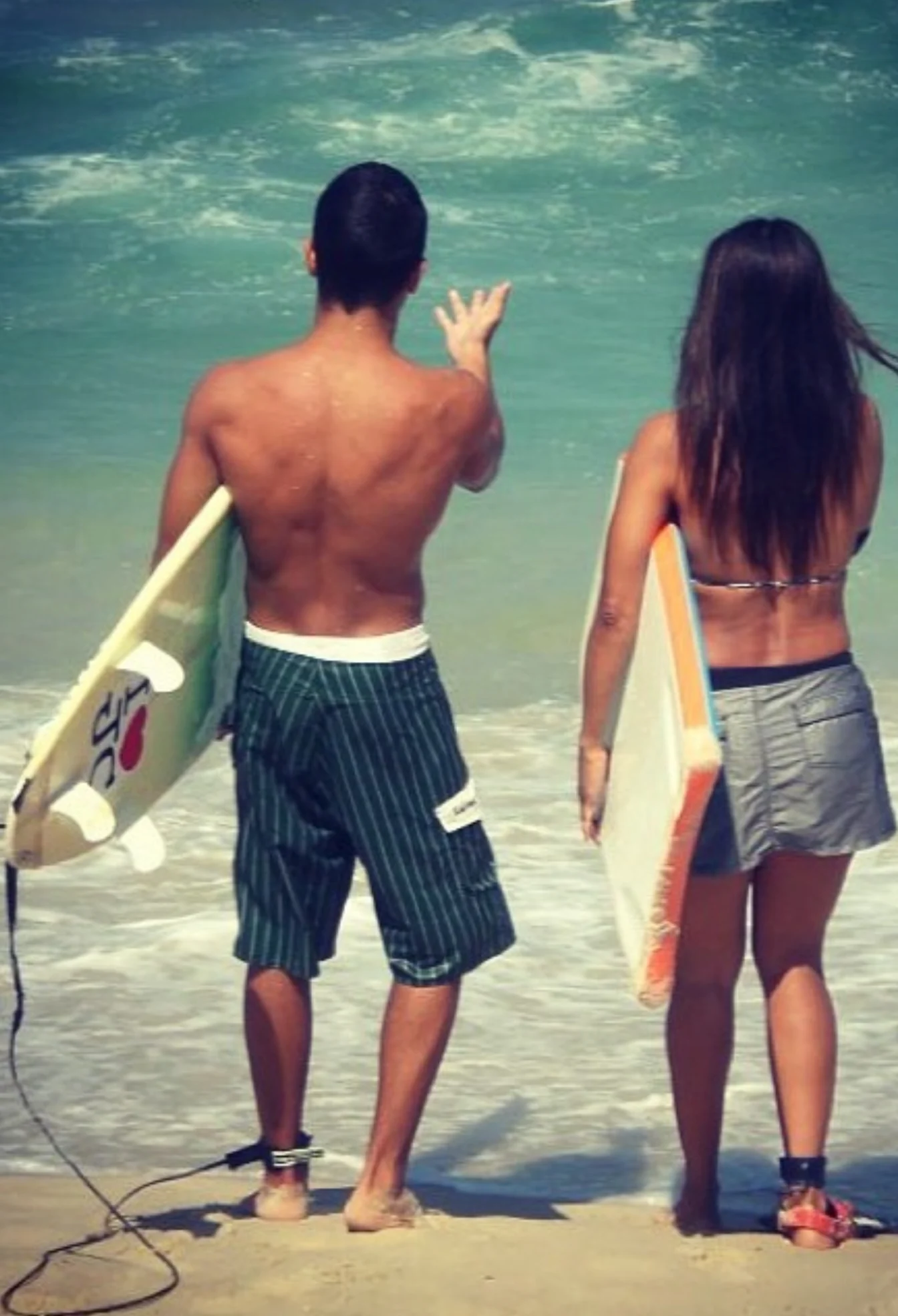 Raphael and a friend from behind holding bodyboards at the shoreline