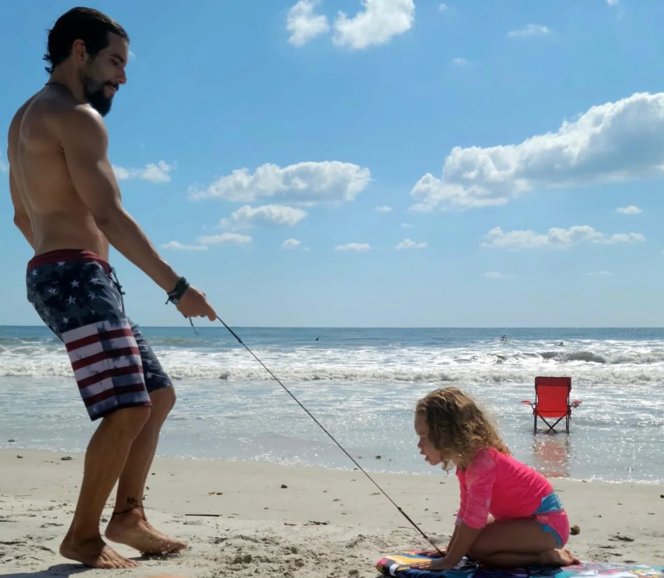 Raphael walking on the beach towing his young daughter on a bodyboard