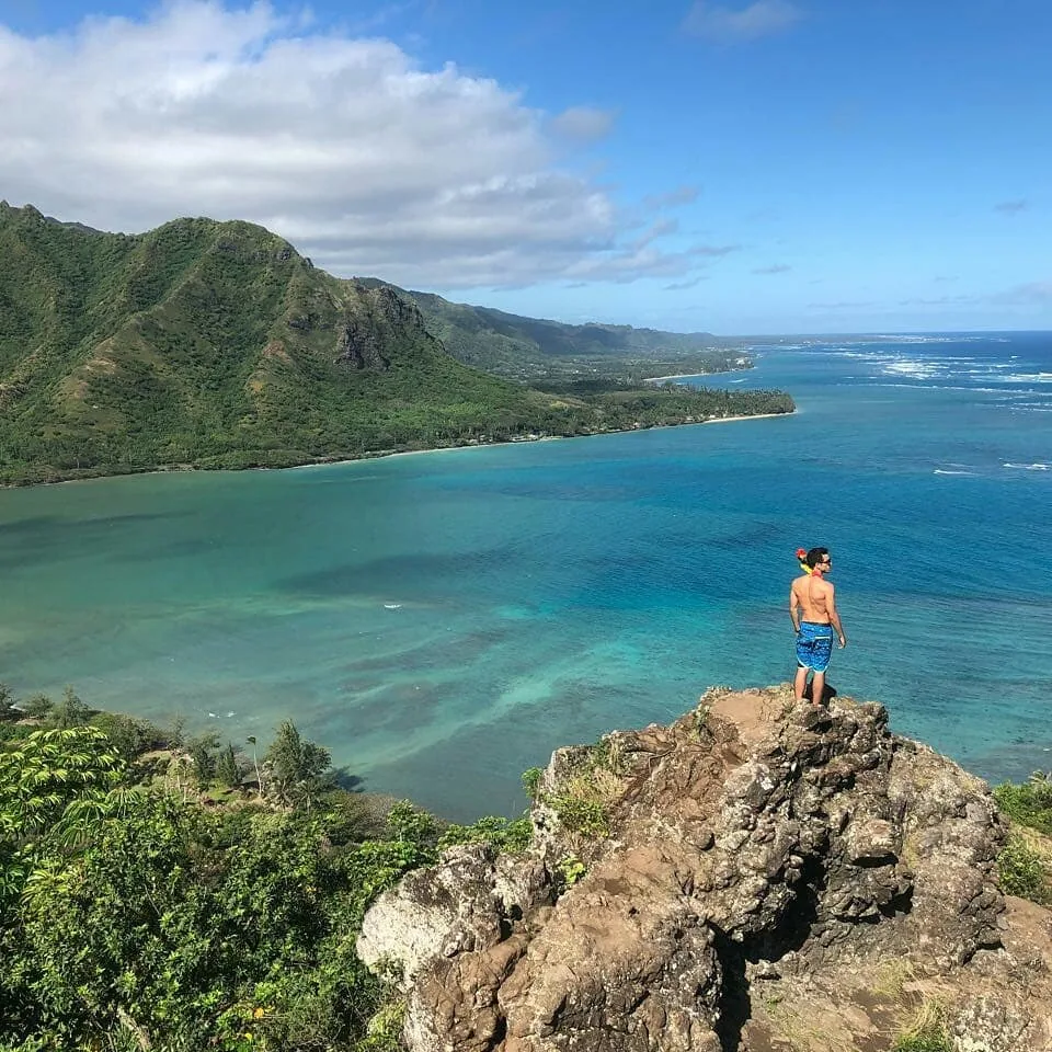 Raphael standing on a rocky cliff above a turquoise bay