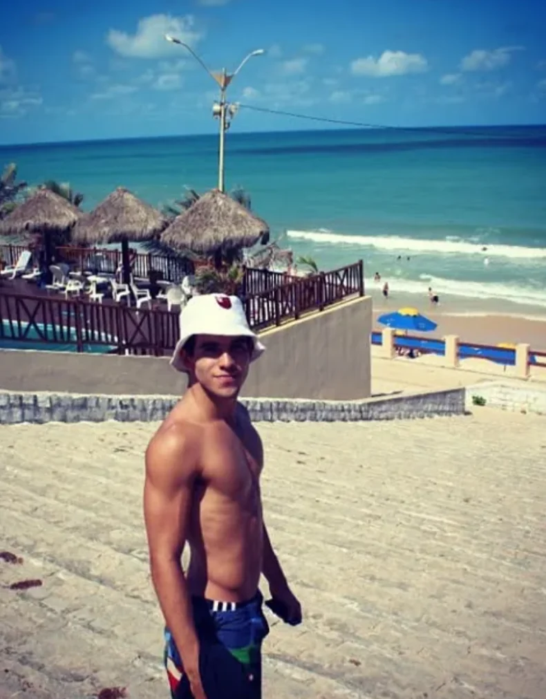 Raphael in a white bucket hat on beach stairs above the ocean