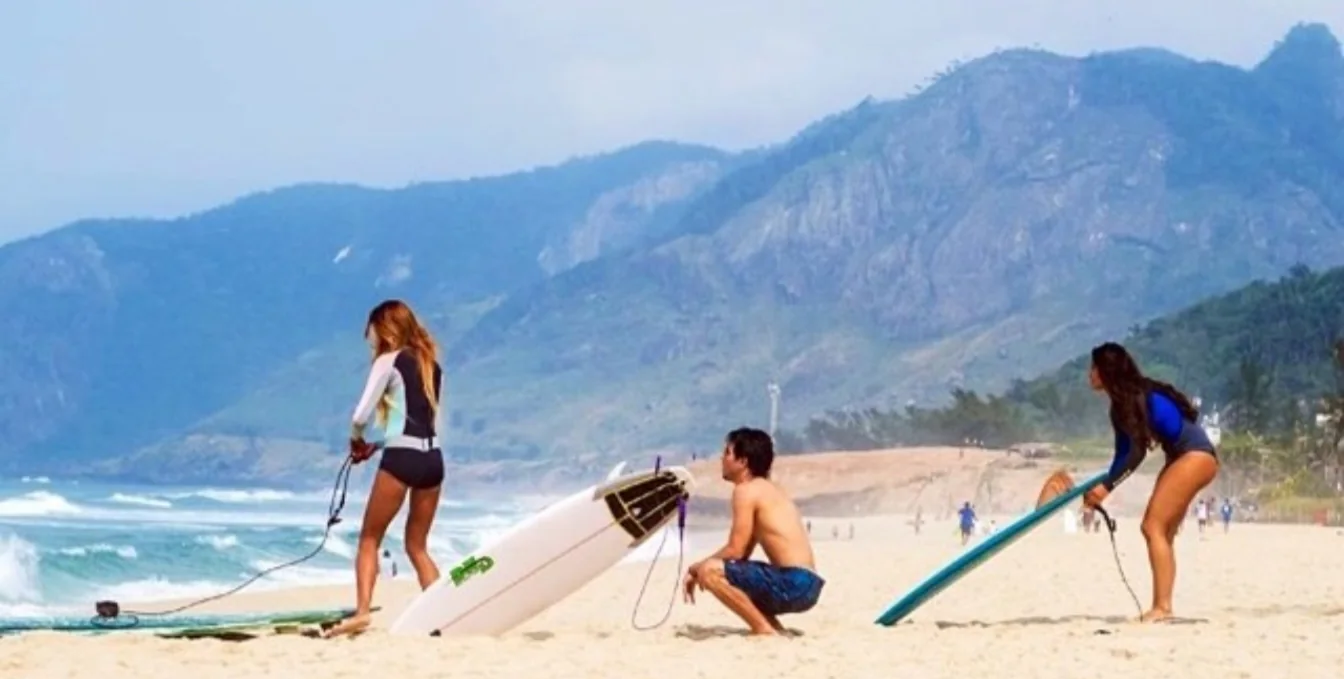 Three surfers on the beach with mountains behind