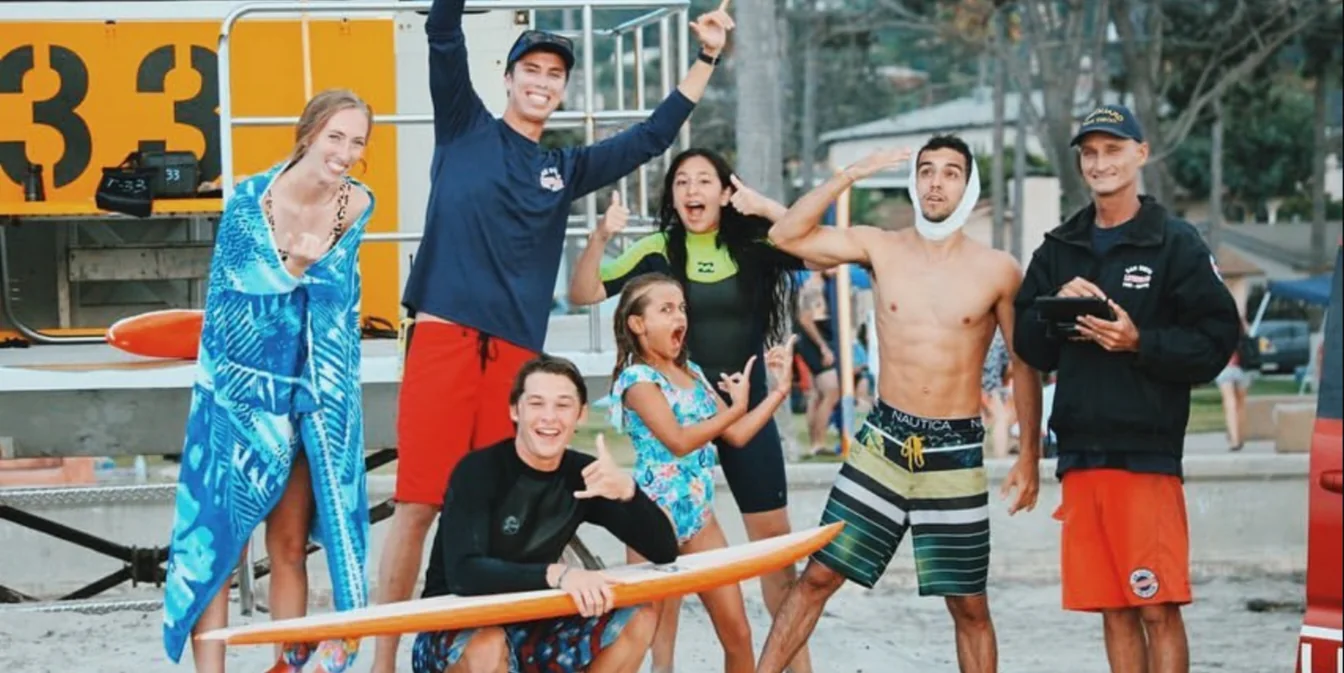 Friends and lifeguards posing on the beach, one with a bandaged jaw