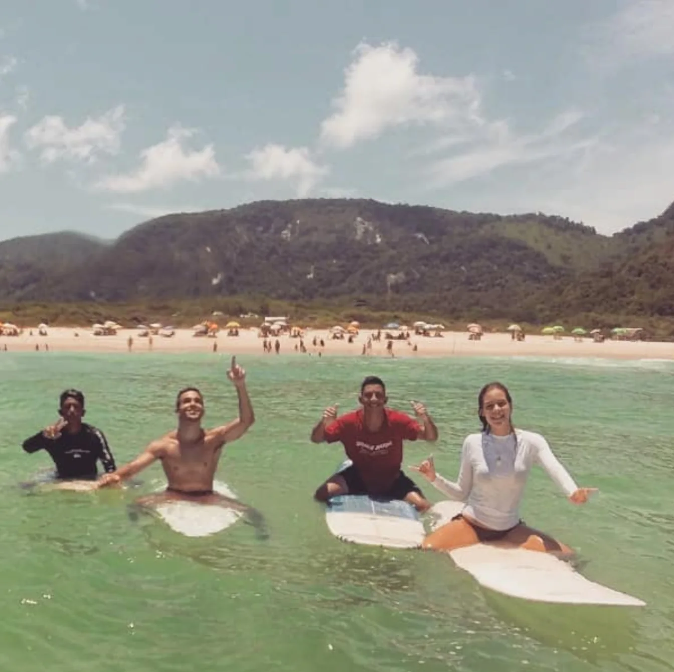 Four friends sitting on surfboards in green water with the beach and mountains behind