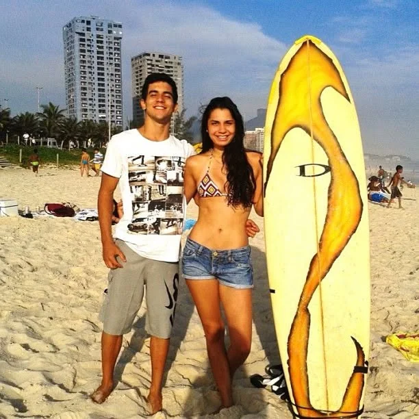 Raphael with a friend on the beach next to a surfboard