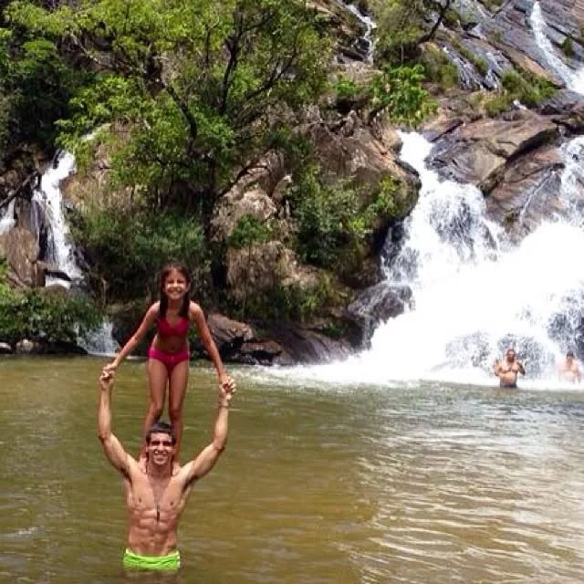 Raphael standing in a waterfall pool lifting a young girl on his hands