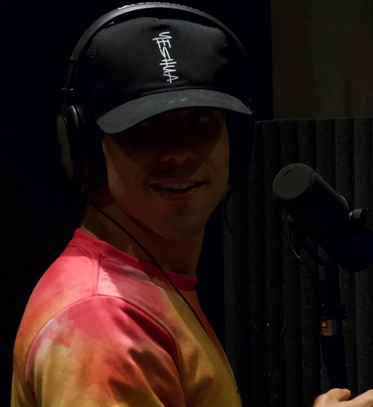 Raphael wearing headphones and a cap in a recording studio next to a microphone
