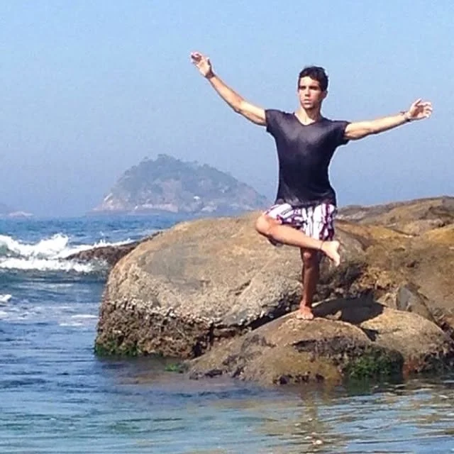 Raphael balancing on one leg on a rock by the sea with arms outstretched