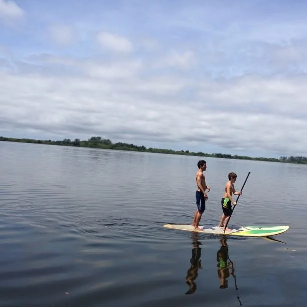 Raphael and a young paddler standing on a paddle board on calm water