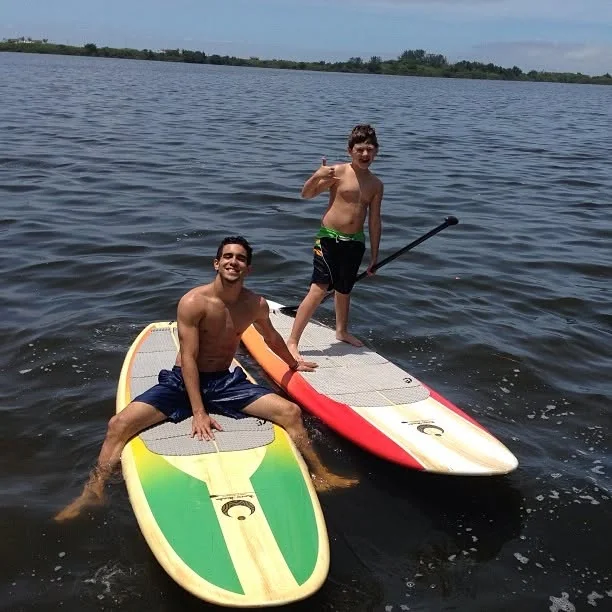 Raphael sitting on a paddle board while a young paddler stands on another