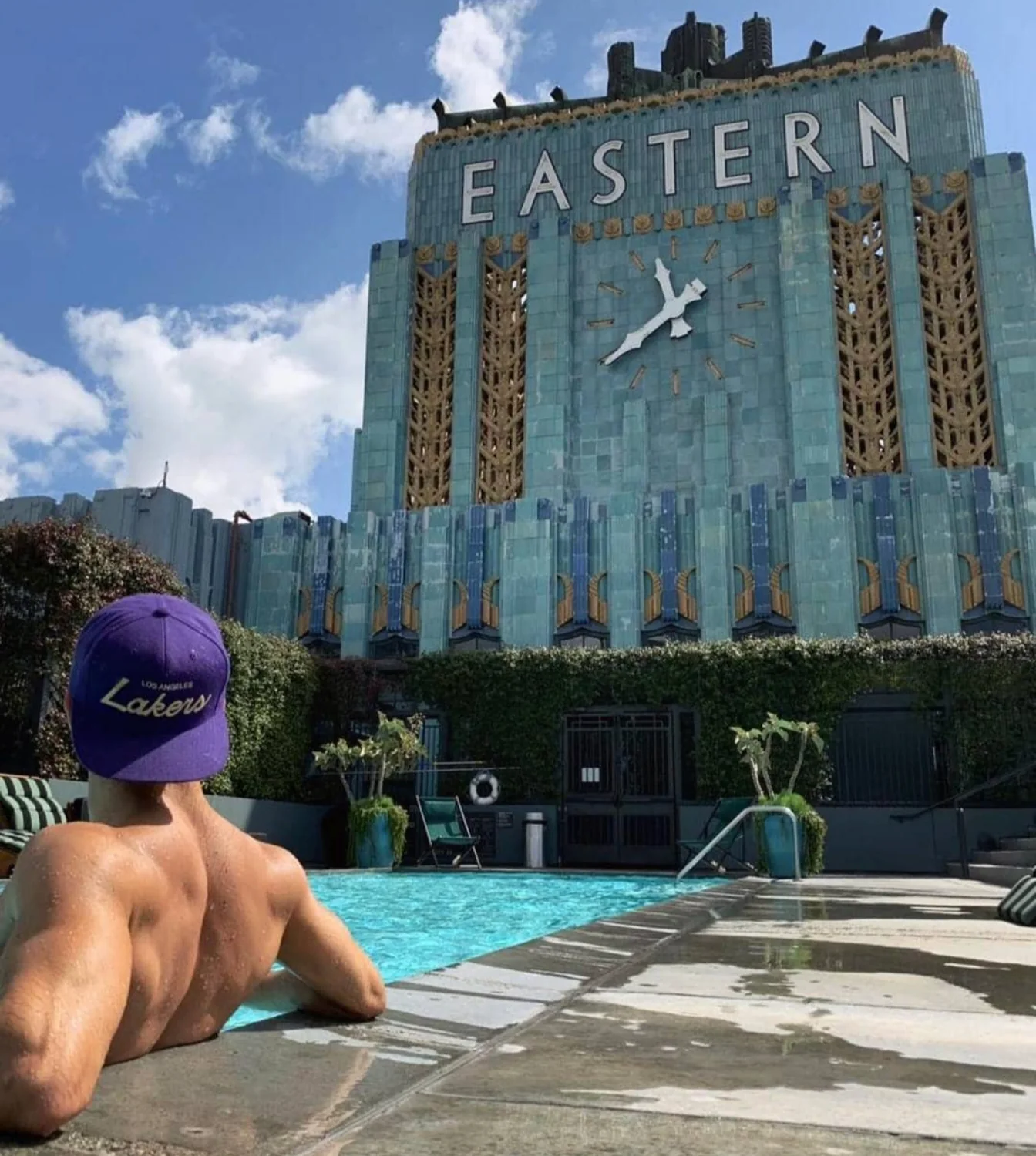 Raphael at a rooftop pool in a purple cap, facing a landmark art deco building